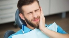 Man in need of emergency dentistry holding cheek in pain